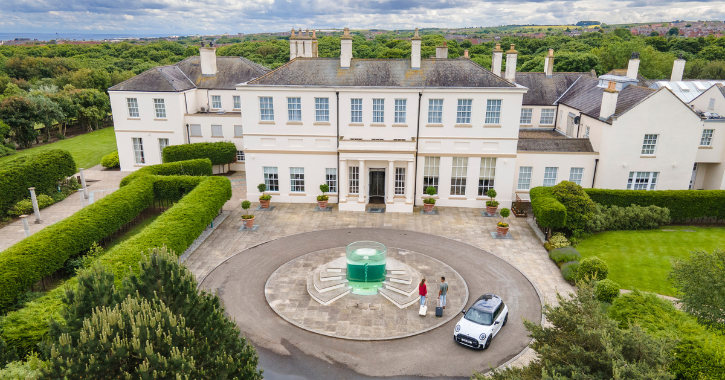 Aerial view of Seahm Hall Hotel with a couple getting out of a car with suitcases arriving at the hotel. 